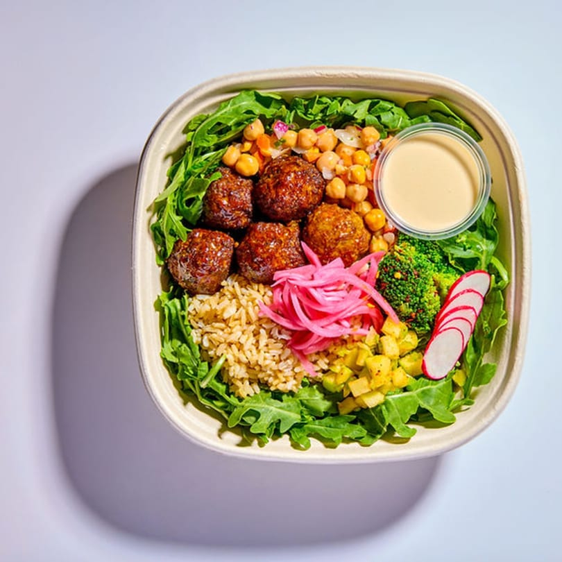 Vitasana healthy bowl with meatballs, brown rice, chickpeas, pickled onions, and dressing.