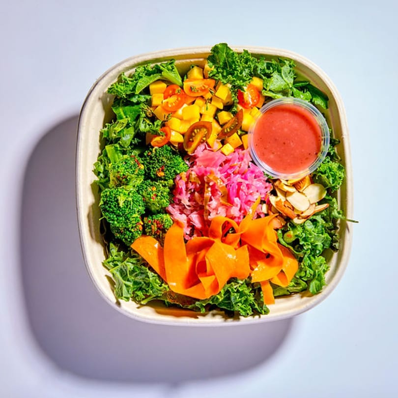 Vitasana's healthy salad bowl with kale, broccoli, mango, tomatoes, pickled cabbage, carrots, almonds, and dressing.