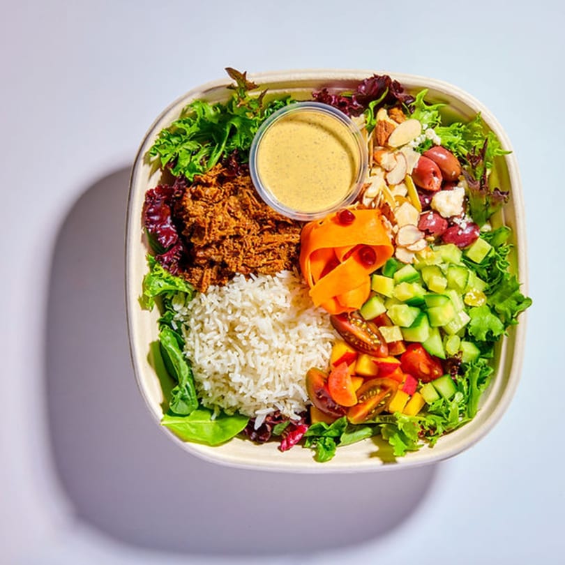 A Vitasana healthy bowl with rice, pulled chicken, salad, vegetables, nuts, and dressing.